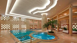 A large indoor swimming pool with a central circular section, surrounded by a tiled floor and a ceiling with recessed lighting. - Guangzhou Marriott Hotel Tianhe (Guangzhou)
