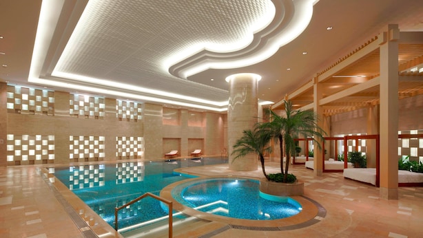 A large indoor swimming pool with a central circular section, surrounded by a tiled floor and a ceiling with recessed lighting. - Guangzhou Marriott Hotel Tianhe (Guangzhou)