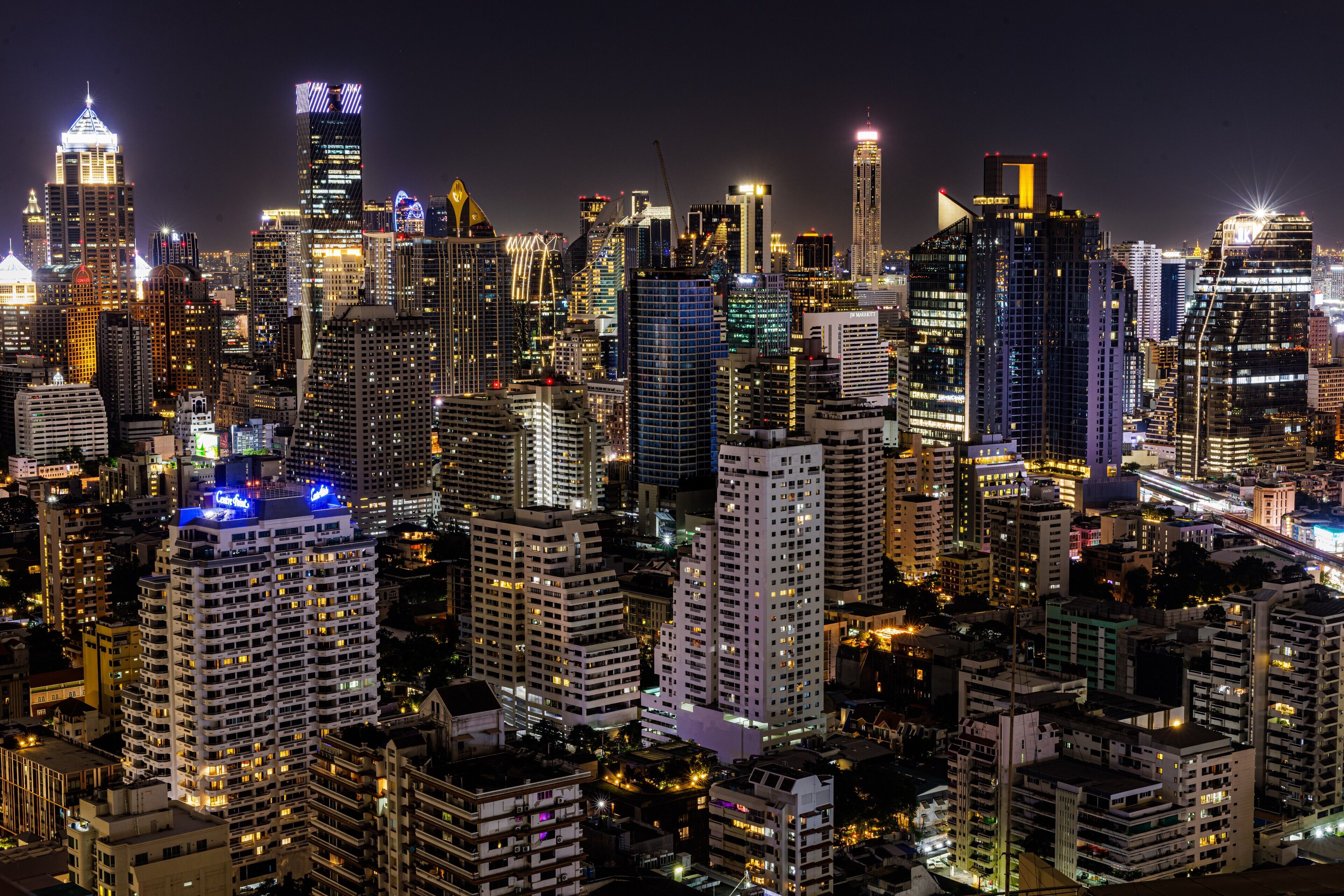 A nighttime cityscape with high-rise buildings, illuminated windows, and a dense urban environment.