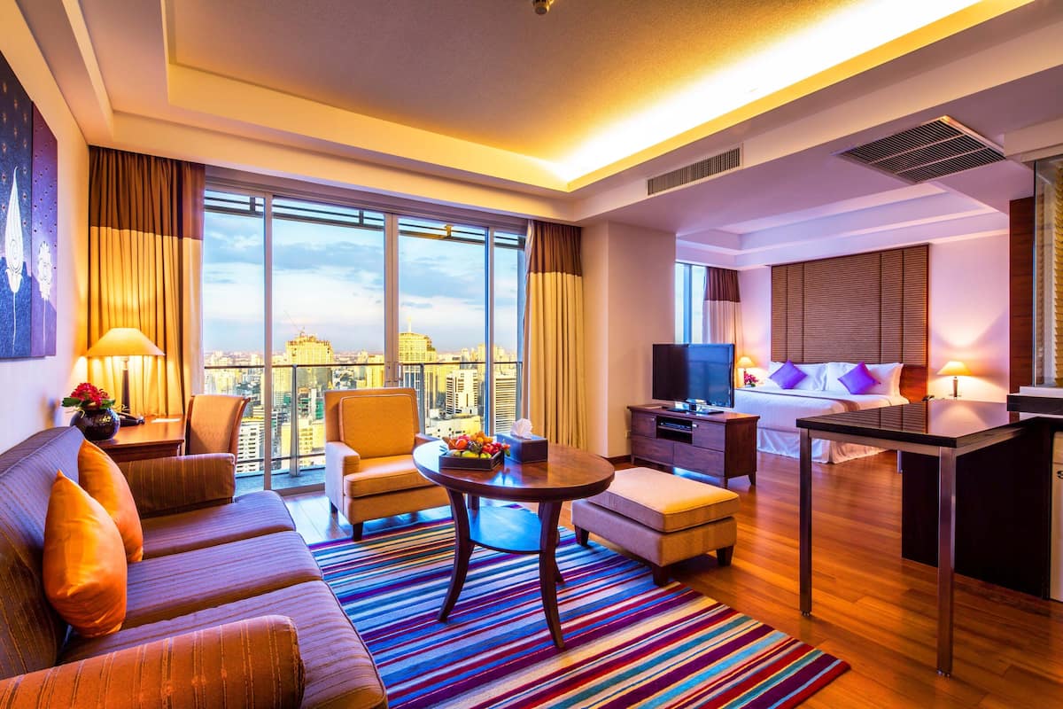 Una habitación de hotel moderna con un ventanal grande, un sofá, una mesa de comedor, un televisor y una pequeña cocina.