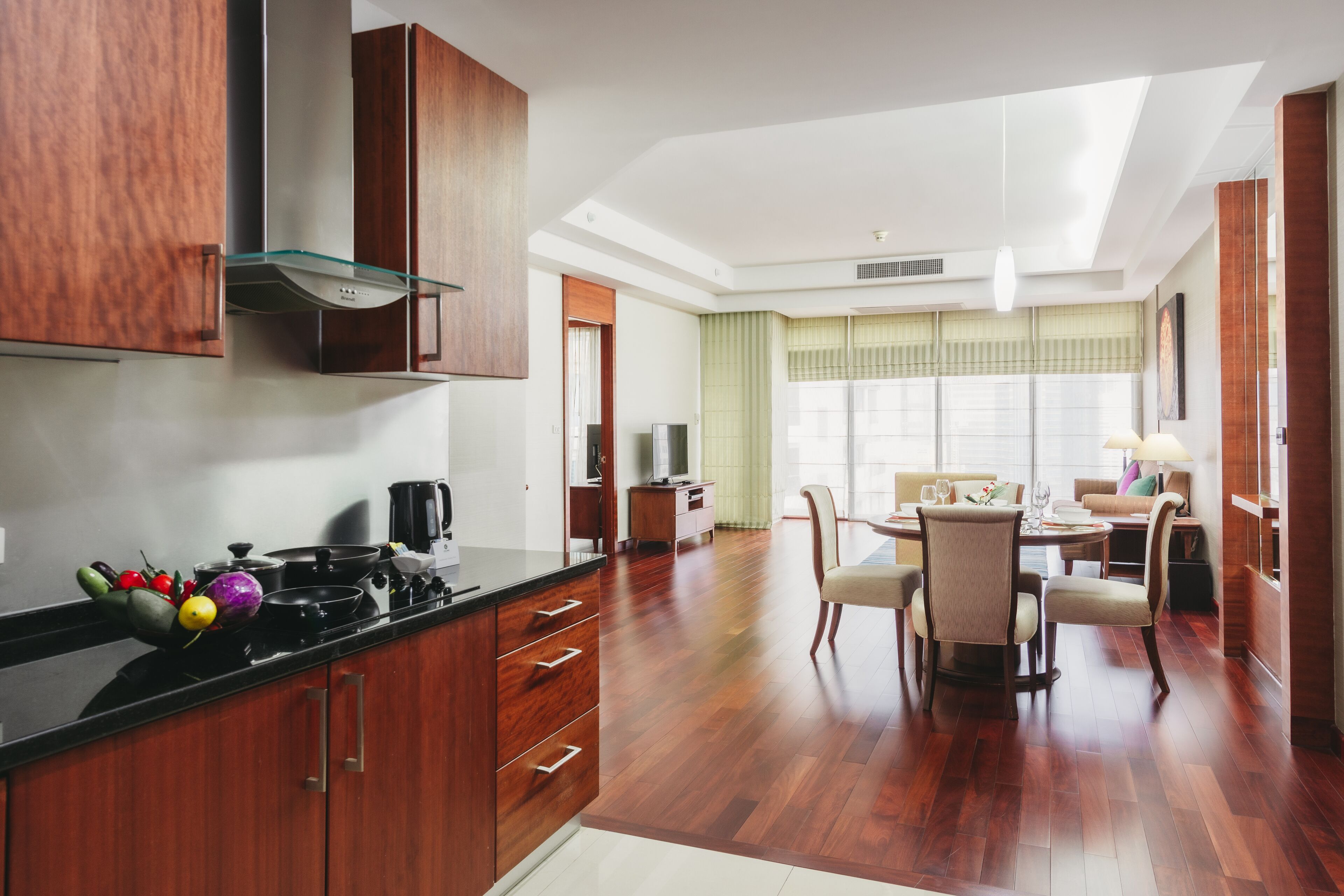 A modern kitchen with wooden cabinets, a dining area with a table and chairs, and a living room with a sofa and a TV.