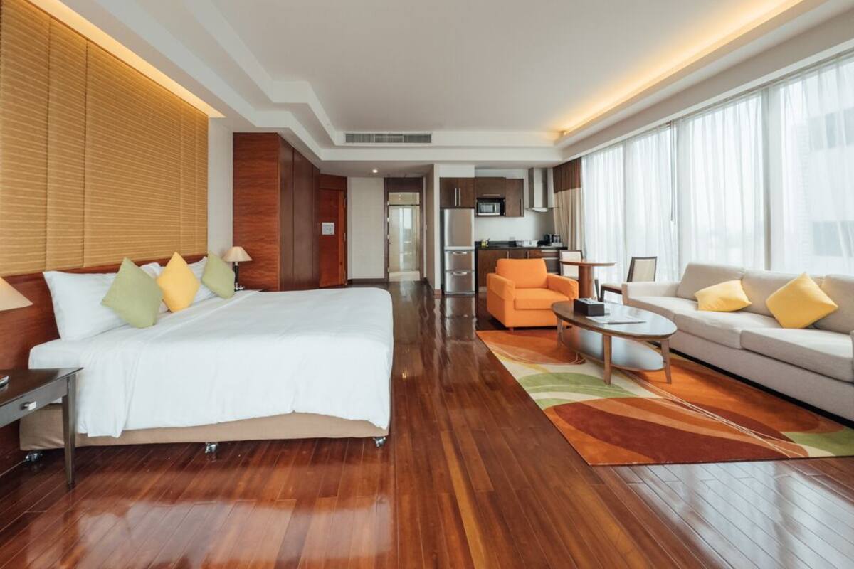 Habitación de hotel con una cama grande, un sofá, una mesa de centro y vistas a la cocina.