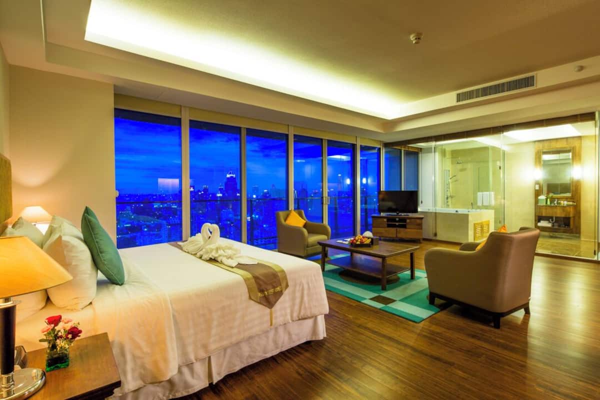 Habitación de hotel moderna con una cama grande, televisión, escritorio y vistas de la ciudad por la noche.