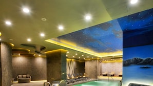 Piscina interna com mural da noite estrelada, cadeiras de descanso e área de spa.