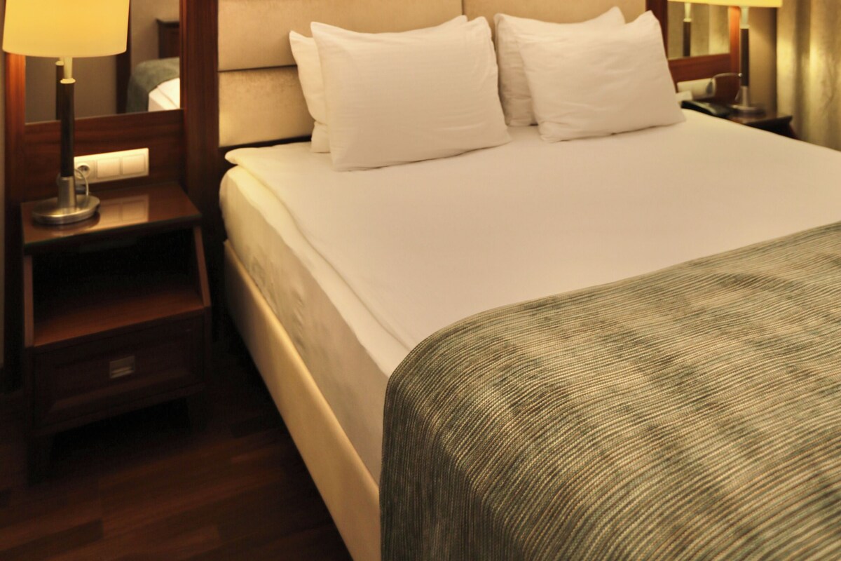 A hotel room with a large bed, bedside lamps, a nightstand, a mirror, and a television.