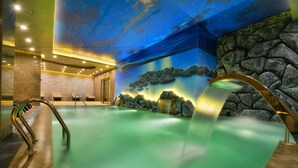 Uma área de spa com piscina verde, cascata e teto que imita um céu estrelado.