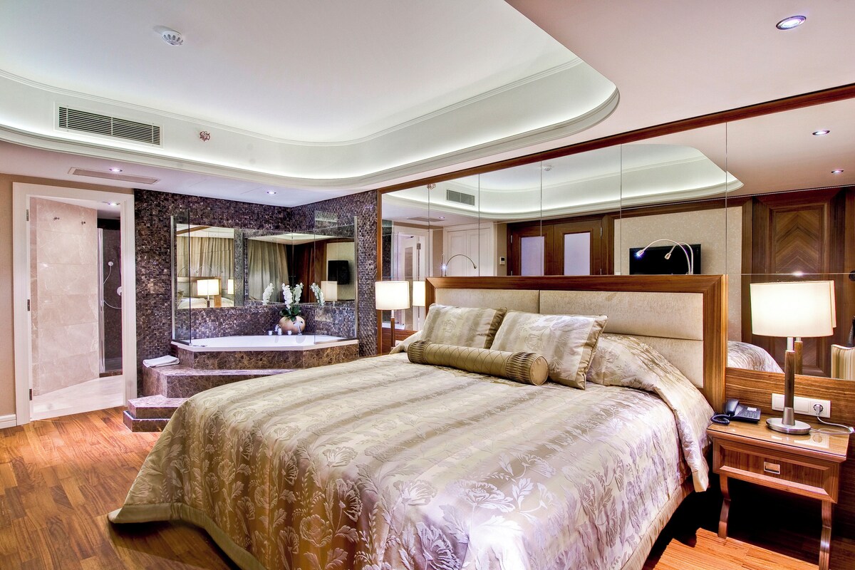 A hotel room with a large bed, a bathroom with a marble wall, and a television.