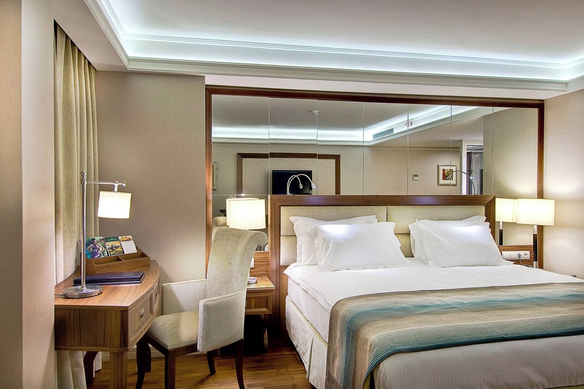 Een hotelkamer met een bed, nachtkastjes, een bureau, een stoel, een lamp en een grote spiegel.