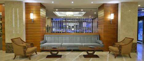 A lobby with a central seating area, wooden panel walls, and a view of parked cars through a glass barrier.
