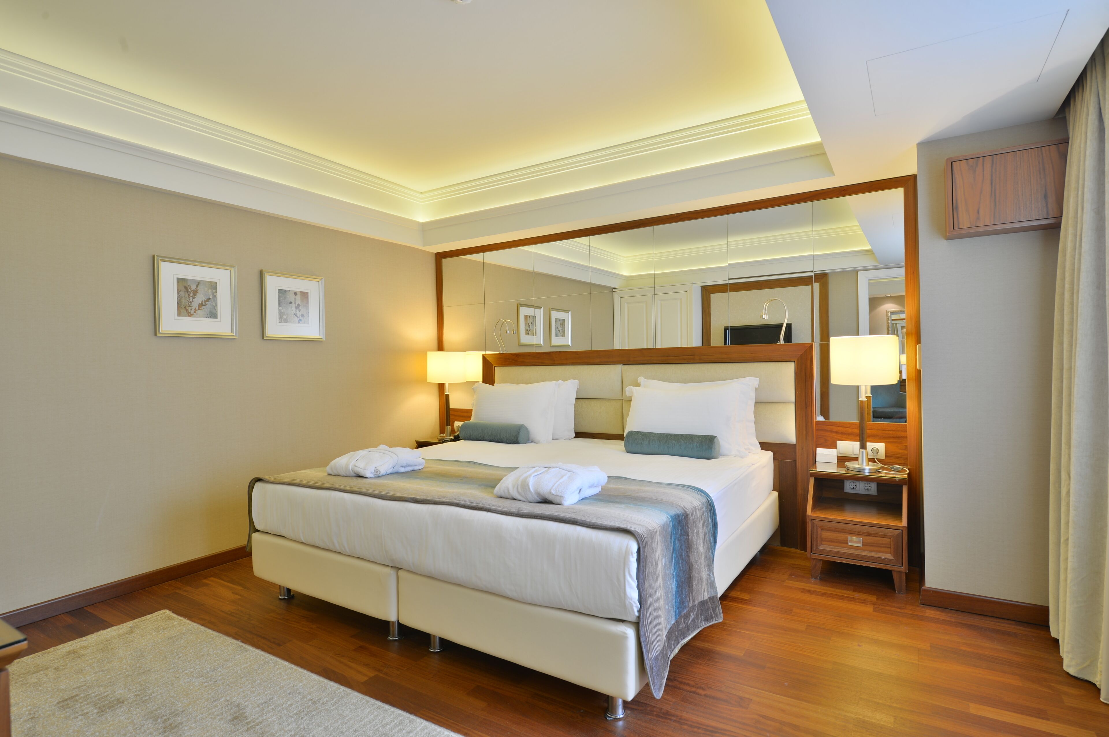 Une chambre d’hôtel avec un grand lit, des tables de chevet, un miroir et des tableaux encadrés au mur.