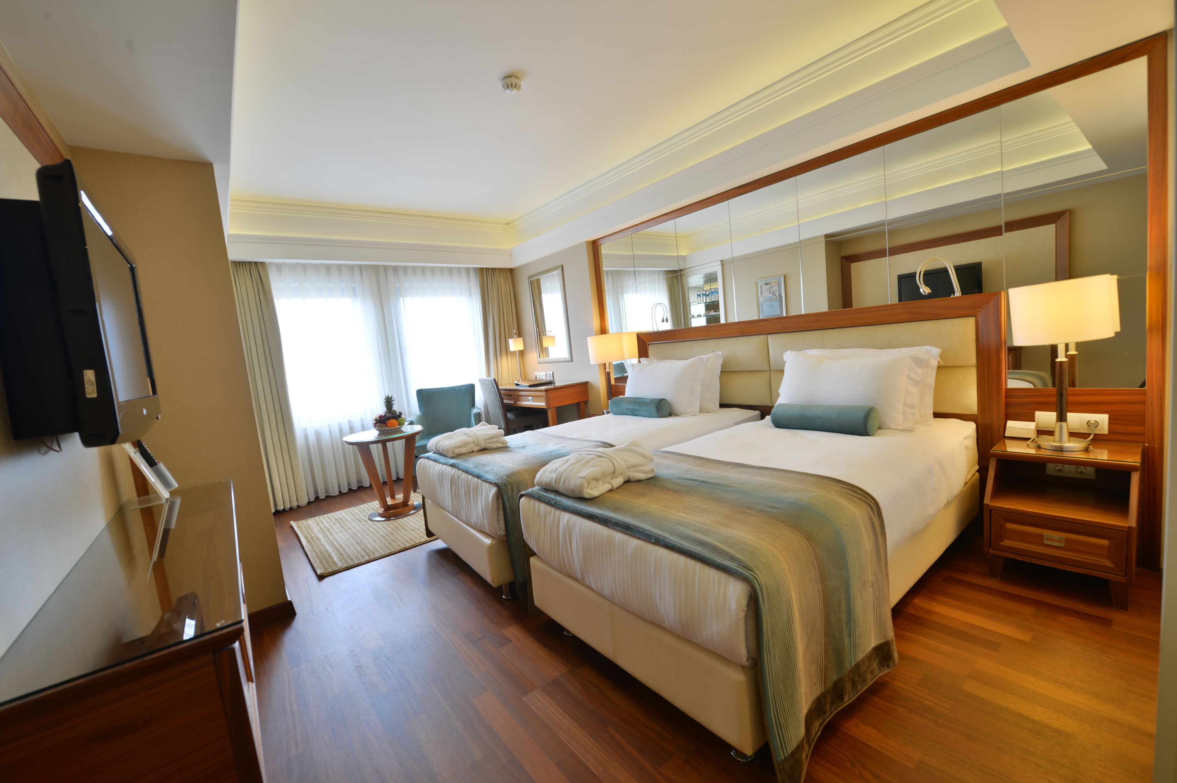 A hotel room with two beds, a TV, a desk, and a mirror.