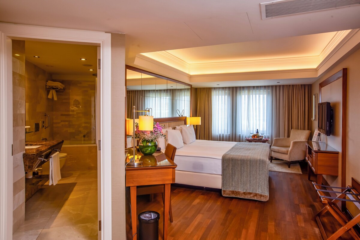 A hotel room with a bed, bedside table, chair, TV, and a bathroom with a shower and toilet.