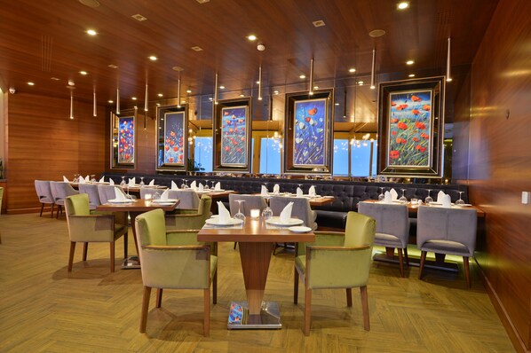 Un restaurante con paneles de madera, varias mesas con sillas y cuadros en las paredes.
