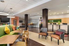 Un hall d’hôtel moderne avec un canapé vert, des tables en bois et un espace bar.
