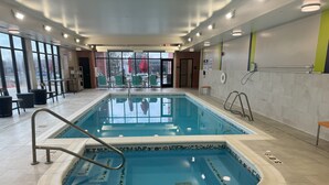 Piscina interior com água cristalina, prancha de mergulho e boia na parede.