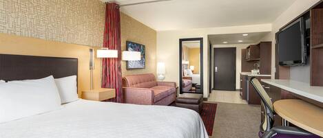 A hotel room with a large bed, a desk with a chair, a TV, and a bathroom visible through an open door.