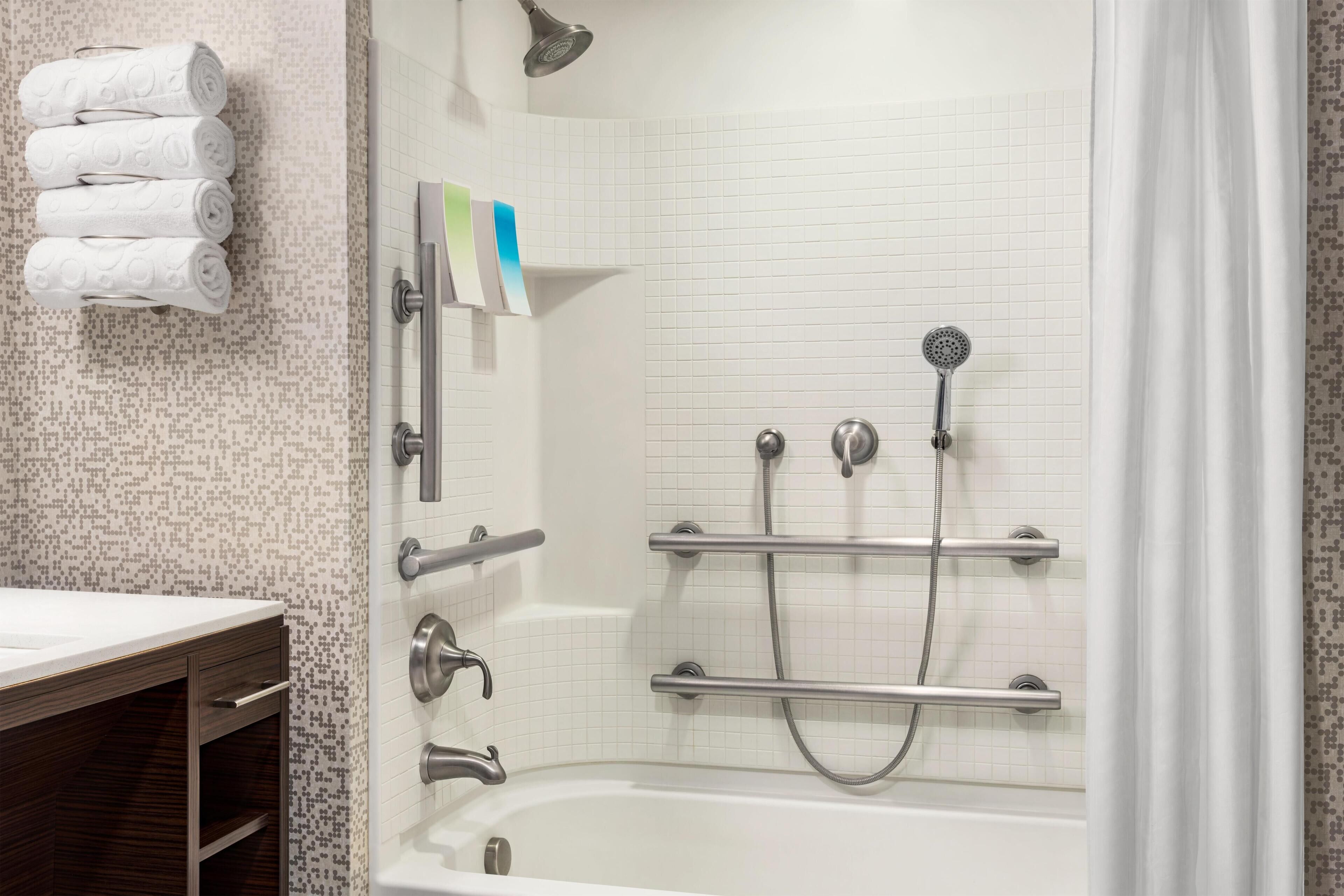 A bathroom with a bathtub, a shower with a handheld showerhead, and a towel rack with folded towels.