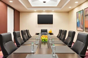 Un salón de conferencias con una mesa larga, sillas de cuero negro, un televisor de pantalla plana y un frutero en el centro.