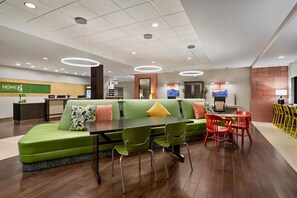 Un moderno vestíbulo de hotel con un sofá verde, una recepción y una zona de comedor con sillas rojas.