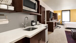 Quarto de hotel moderno com cozinha, cama e escrivaninha.
