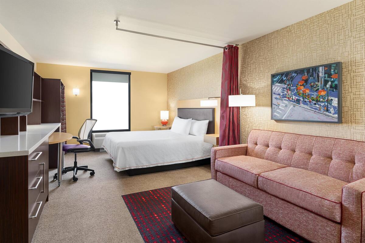 Una habitación de hotel con cama, sofá, escritorio, silla y televisor.