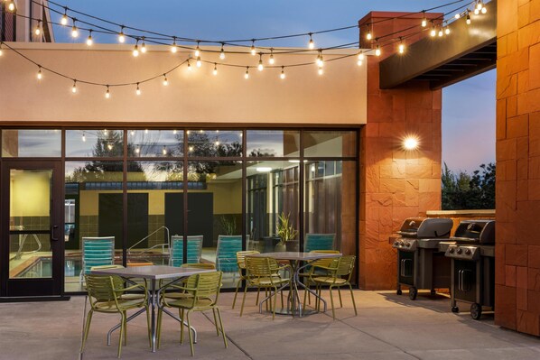 Un patio al aire libre con cerramiento de vidrio, luces colgantes y una zona de barbacoa.