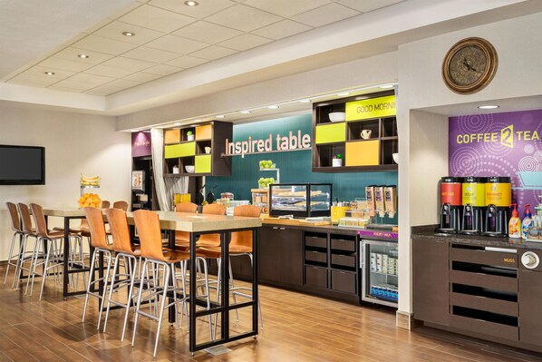 A modern cafe with a central table, bar area, and coffee machines.