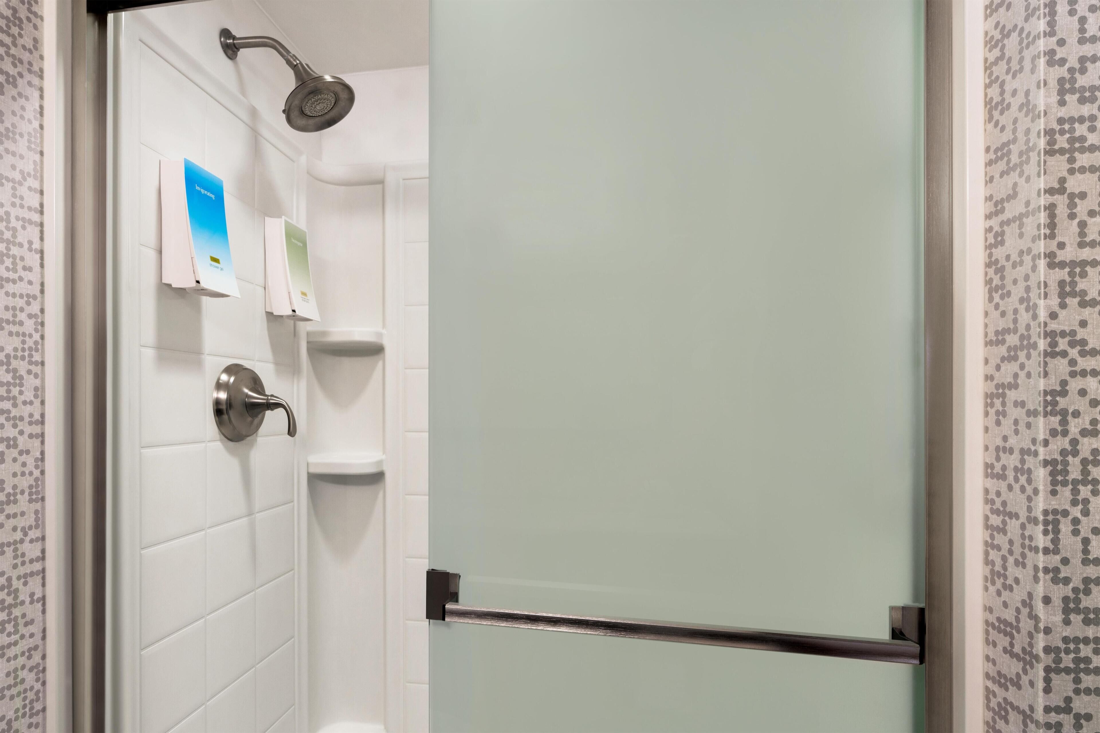 Un espace douche doté d’une porte en verre, d’un pommeau de douche et d’une barre d’appui.