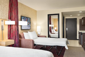 Habitación de hotel con dos camas, un espejo grande, un cuadro en la pared y un baño visible a través de una puerta abierta.