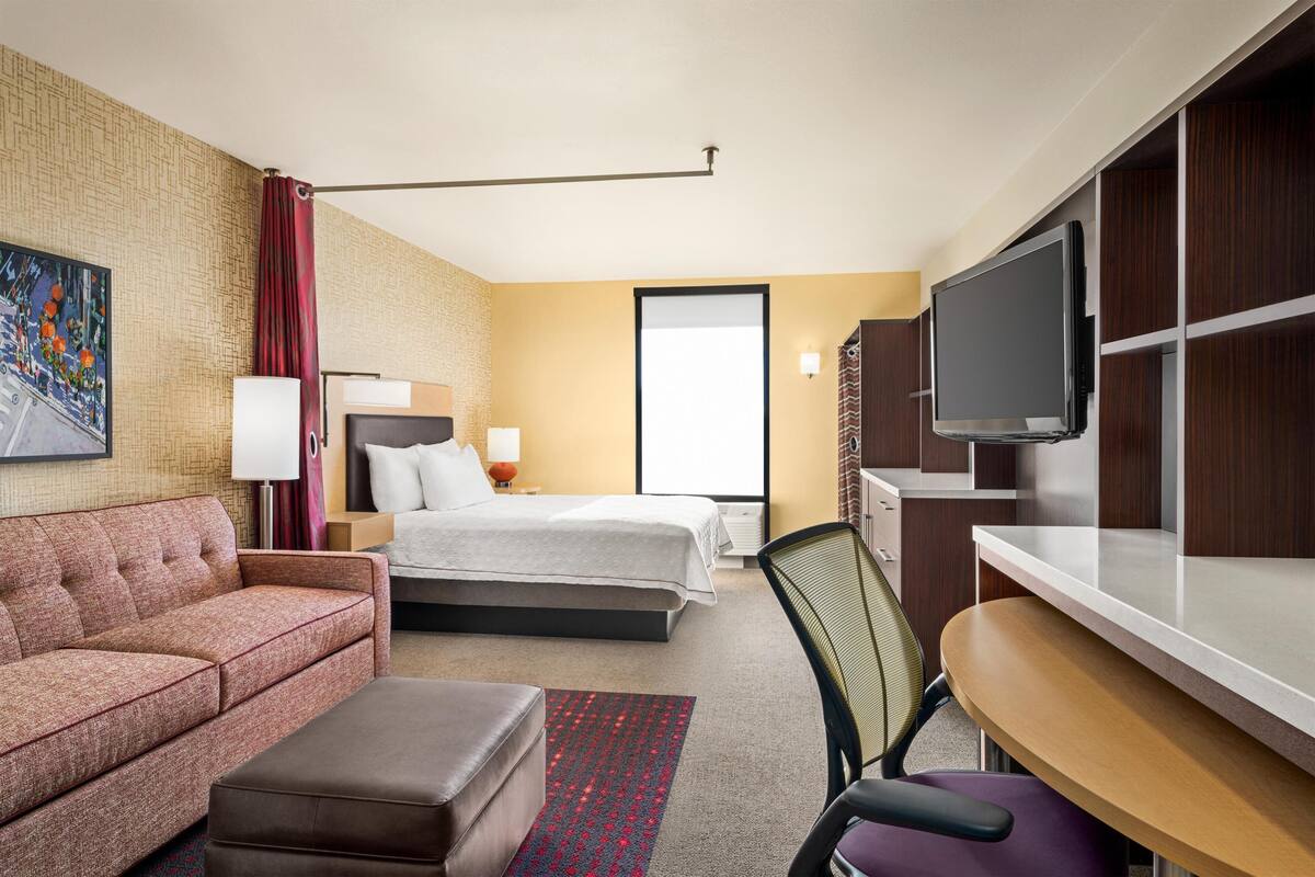 Una habitación de hotel con cama, sofá, escritorio, televisor y un cuadro en la pared.