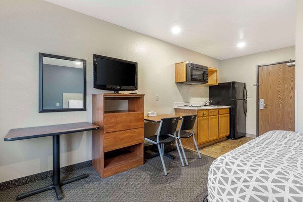 A compact hotel room with a kitchenette, a bed, a desk with a chair, a television, and a mirror. - WoodSpring Suites Raleigh Garner (Garner)