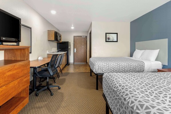 A hotel room with a bed, a desk with a chair, a TV, a microwave, and a door. - WoodSpring Suites Raleigh Garner (Garner)