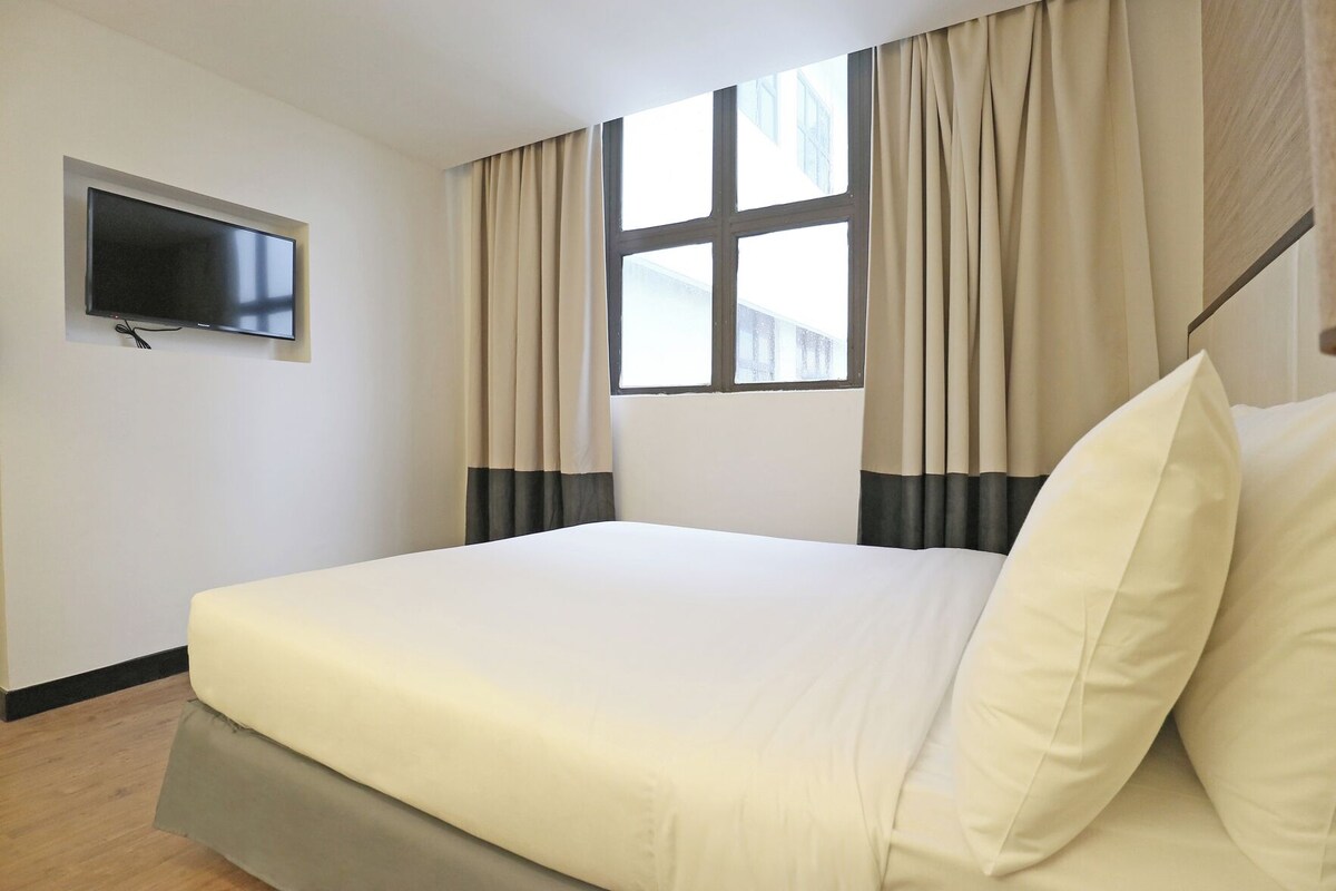 Ein Hotelzimmer mit Bett, Vorhängen, einem Fenster und einem an der Wand befestigten Fernseher.