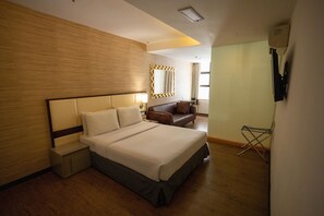 A hotel room with a large bed, a nightstand, a seating area with a sofa, a mirror, and a window with curtains.