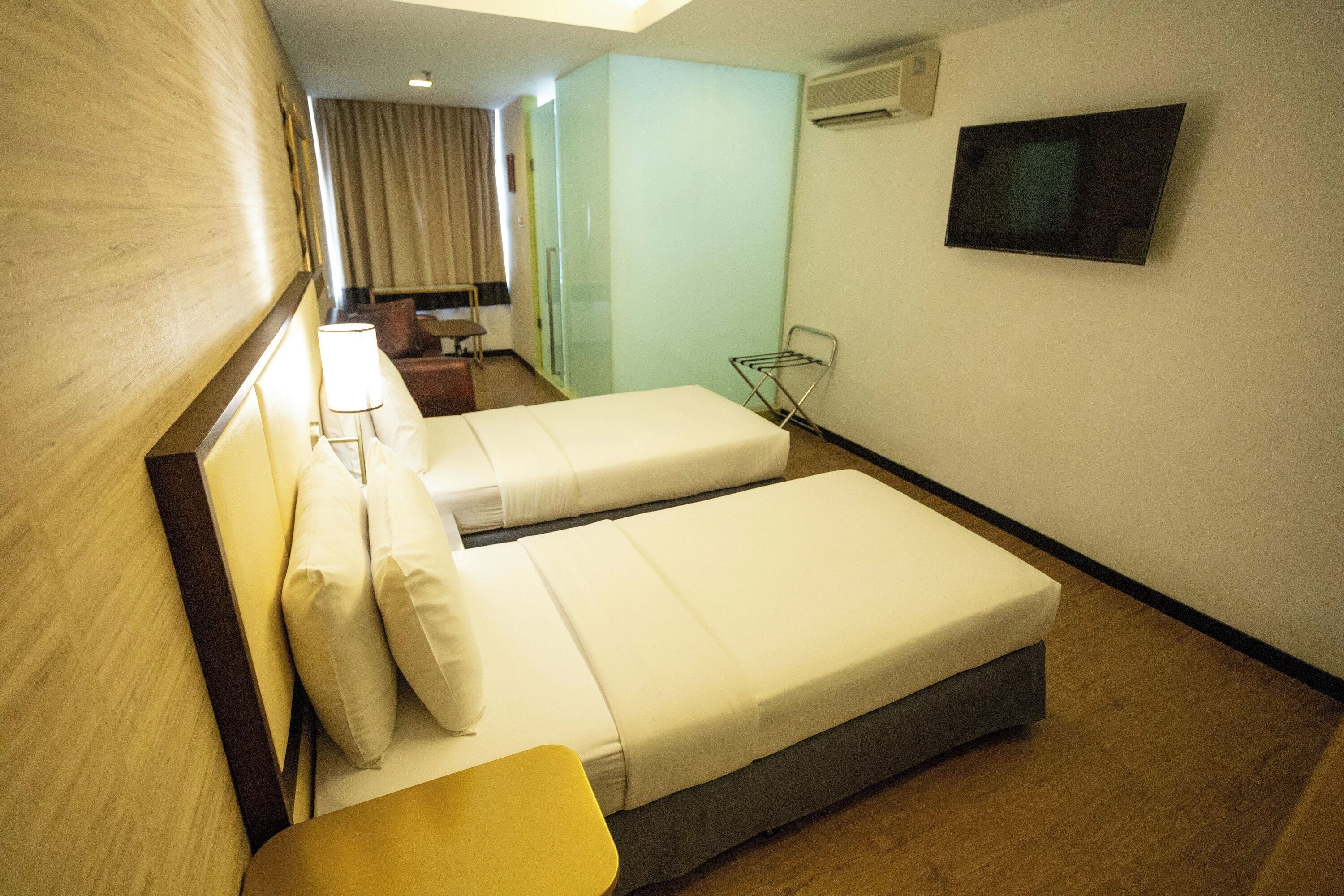A hotel room with two beds, a desk, a chair, a TV, and an air conditioning unit.
