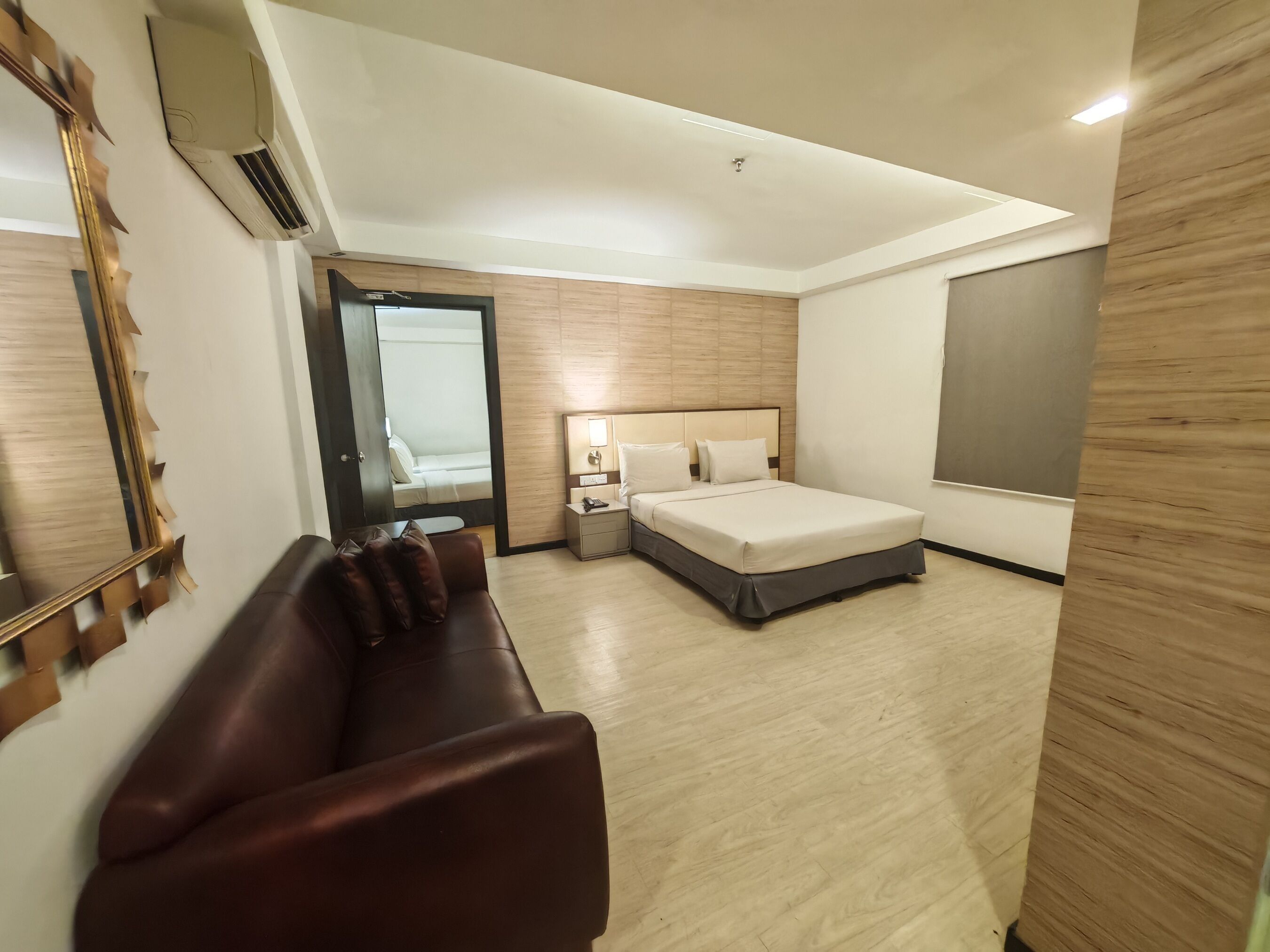 Ein modernes Hotelzimmer mit Bett, Nachttisch, Spiegel, Holzboden und einem großen Fenster.