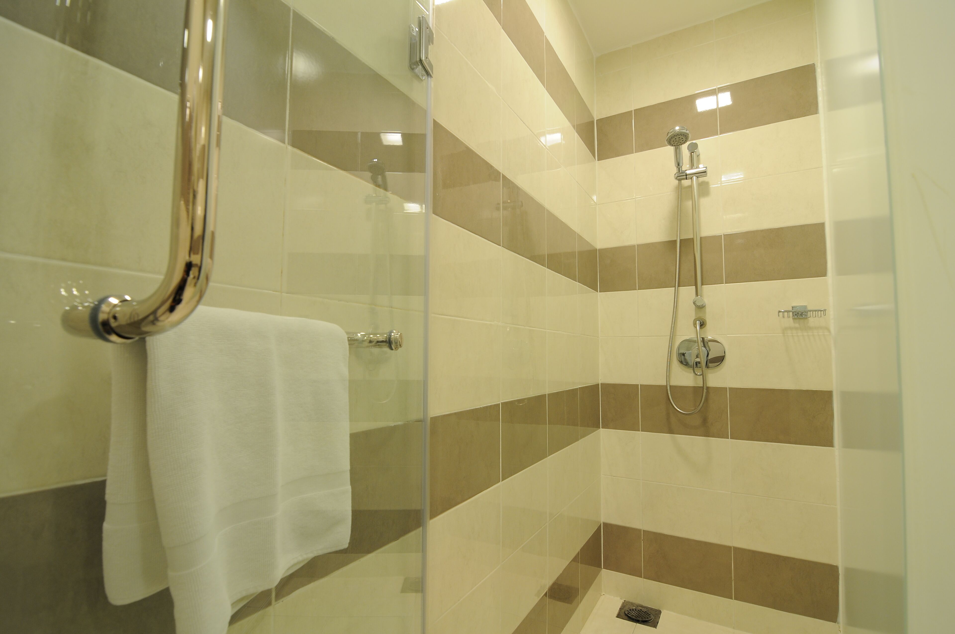 Un baño moderno con cabina de ducha de vidrio, una toalla blanca y un cabezal de ducha.
