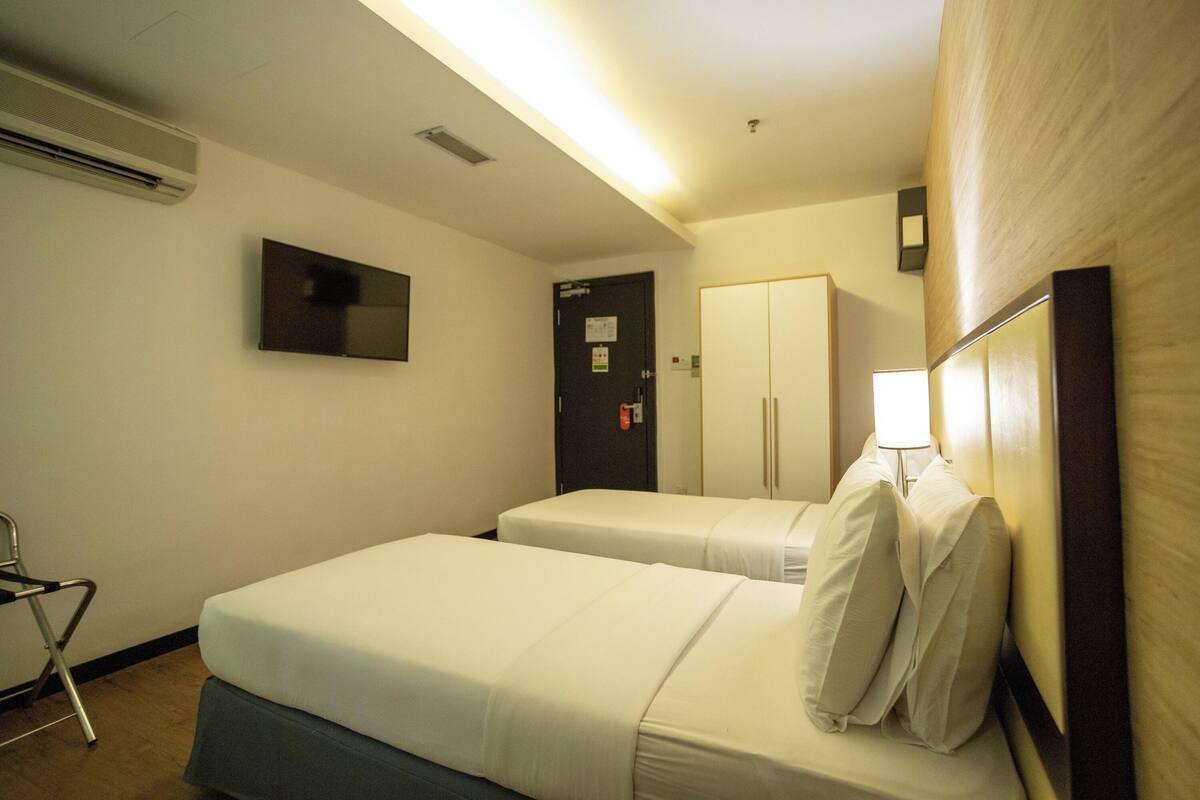 A hotel room with two beds, a TV, a wardrobe, and a chair.