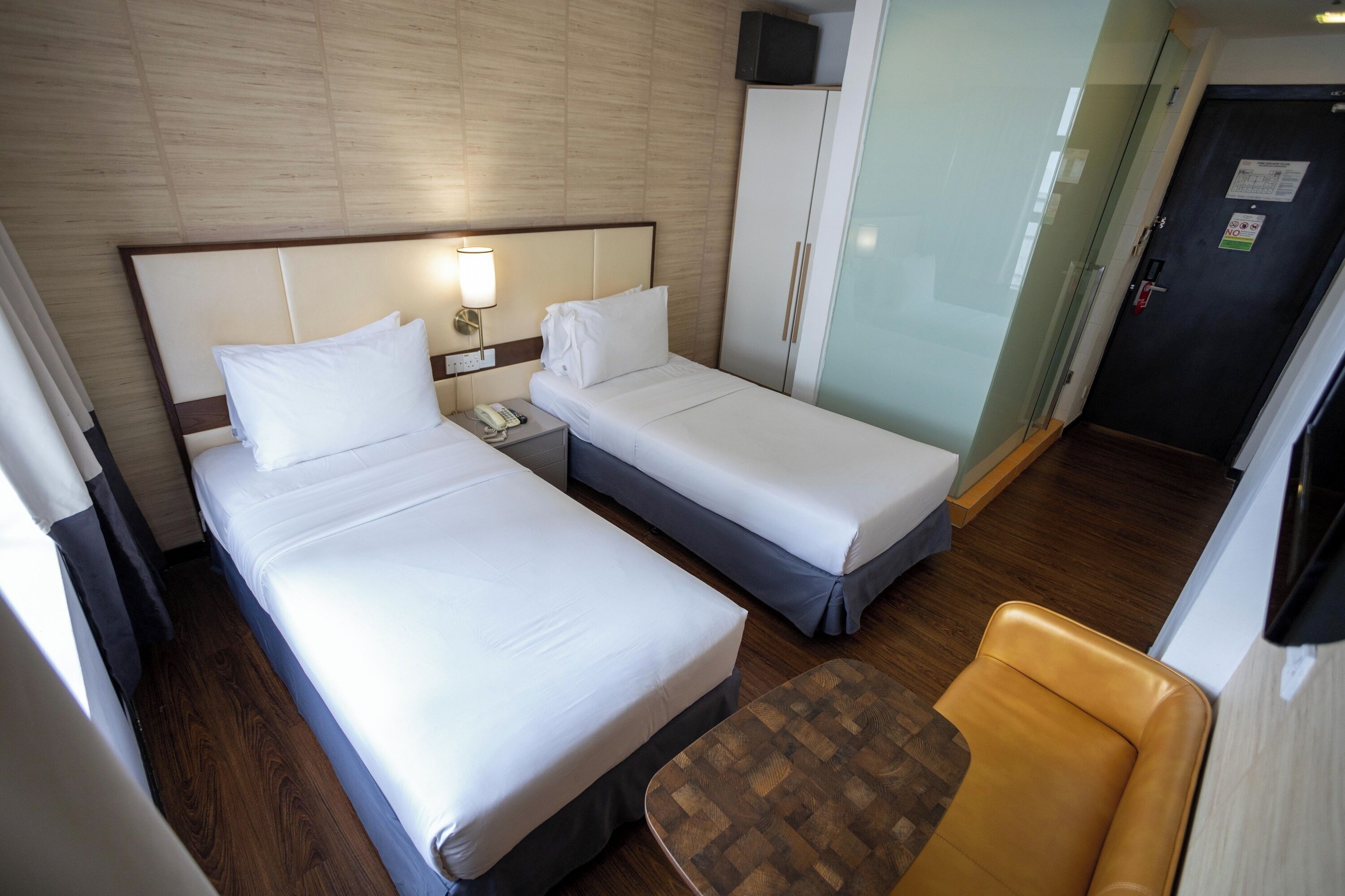 Habitación de hotel con dos camas, una mesita de noche con lámpara, un armario, una silla y un televisor.