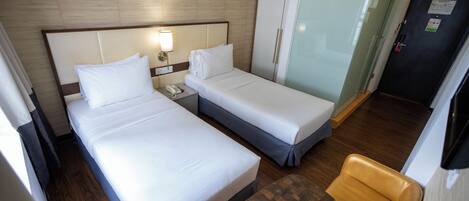 Habitación de hotel con dos camas, una mesita de noche con lámpara, un armario, una silla y un televisor.