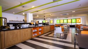 A modern cafe with a central counter, multiple seating areas, and a checkered floor pattern.