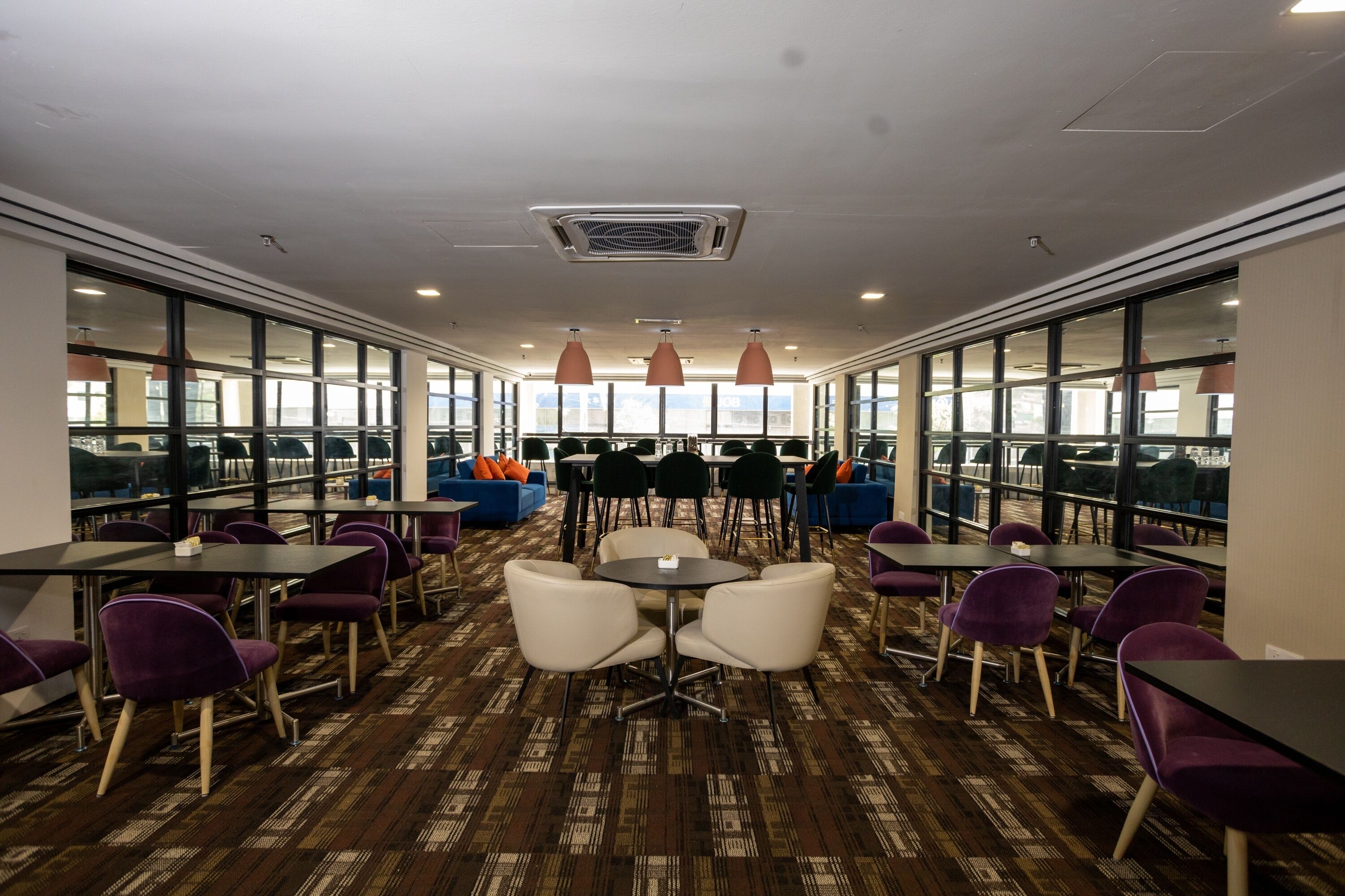 A conference room with tables and chairs, large windows, and pendant lighting.