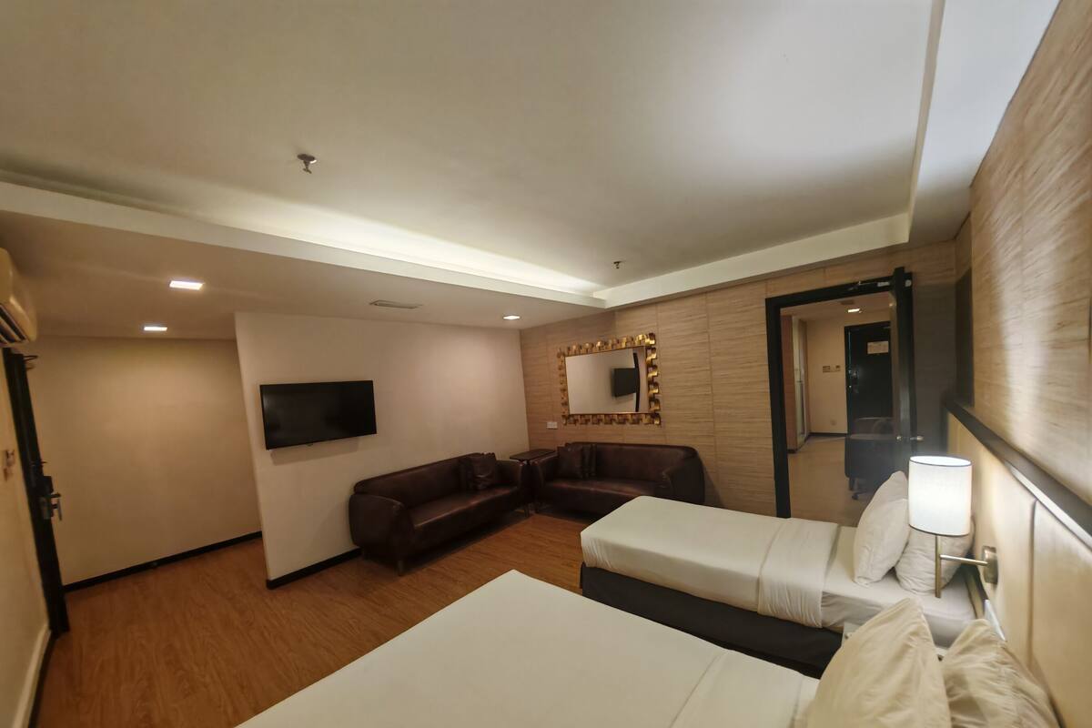 A hotel room with two single beds, a sofa, a TV, and a mirror.
