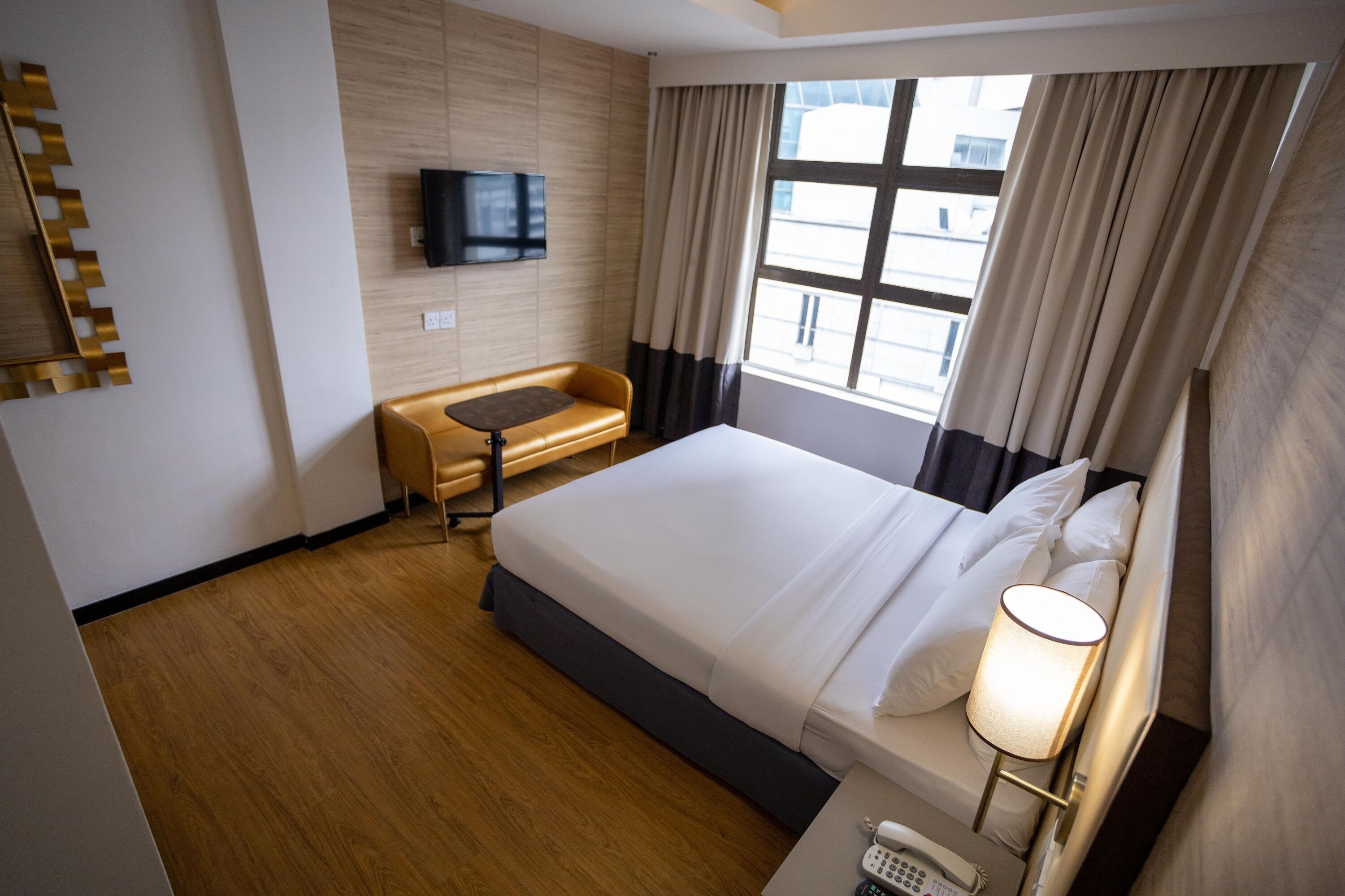Habitación de hotel con una cama grande, un escritorio, un televisor montado en la pared y una ventana con cortinas.