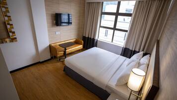 Habitación de hotel con una cama grande, un escritorio, un televisor montado en la pared y una ventana con cortinas.