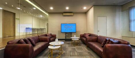 A conference room with leather sofas, small round tables, and a large screen displaying 'Citrus JALAN STATION JOHOR BAHRU'.
