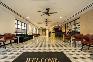 Eine Hotellobby mit einer Rezeption, einer Sitzecke und einer Fußmatte mit dem Schriftzug 'WELCOME'.
