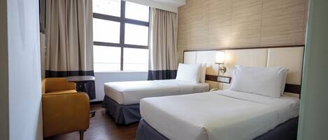 Een hotelkamer met twee bedden, een bank, een klein tafeltje en een raam met gordijnen.