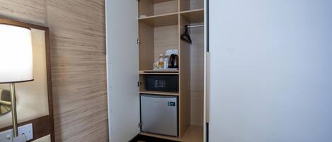 A compact hotel room with a kitchenette, a small refrigerator, a microwave, and a coffee maker on the counter.
