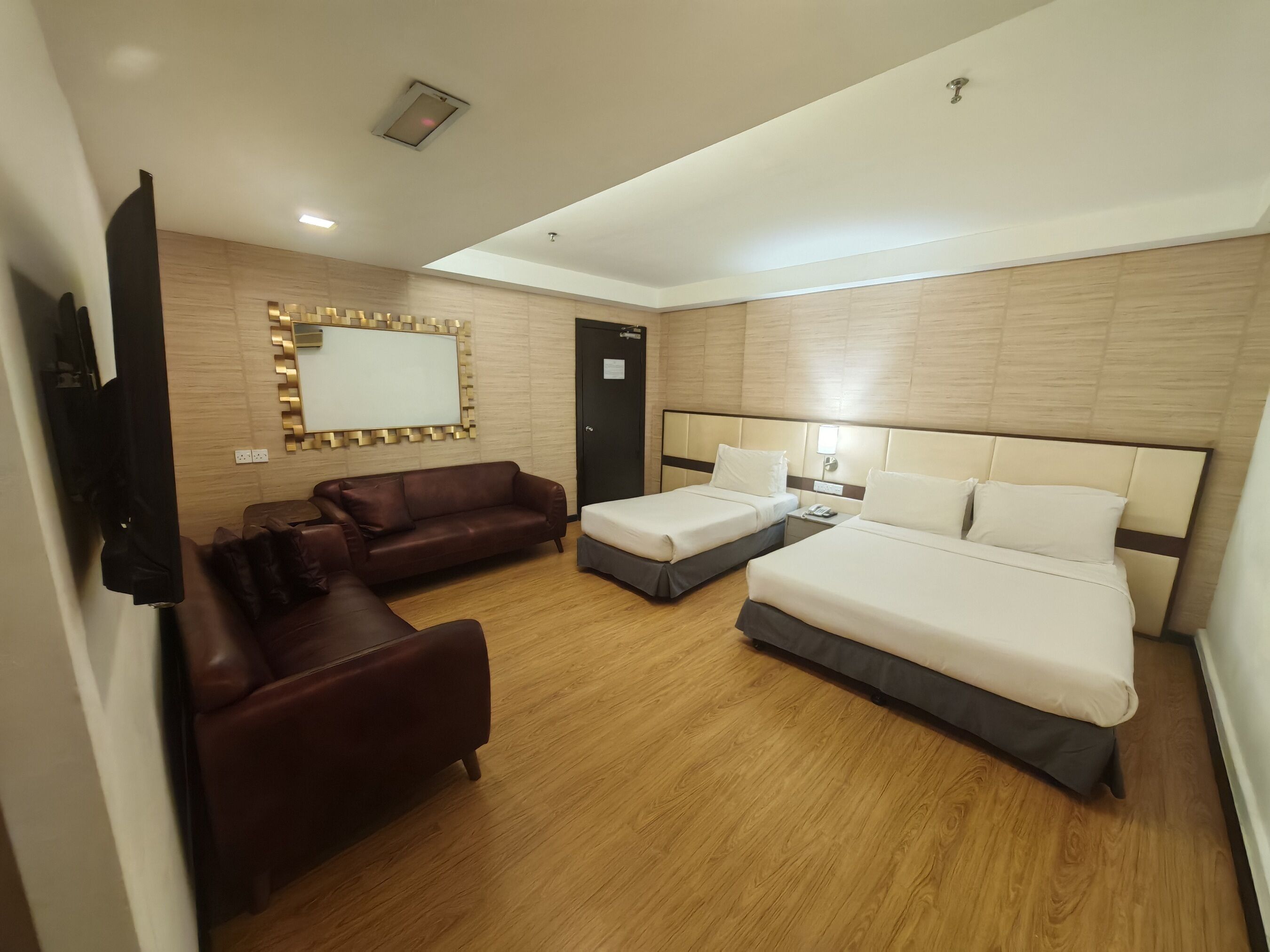 Une chambre d’hôtel avec un canapé, deux lits simples, une petite table, un miroir et un luminaire.
